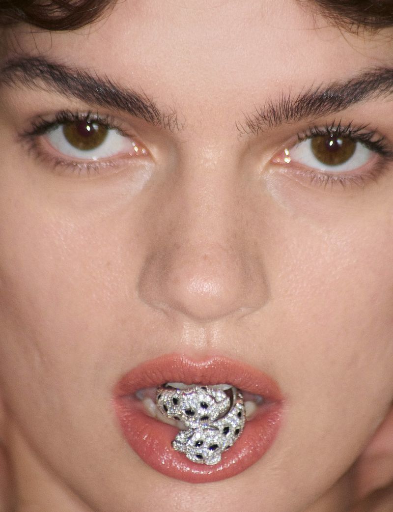 Extreme close-up portrait of a model holding a diamond-encrusted panther ring between her lips