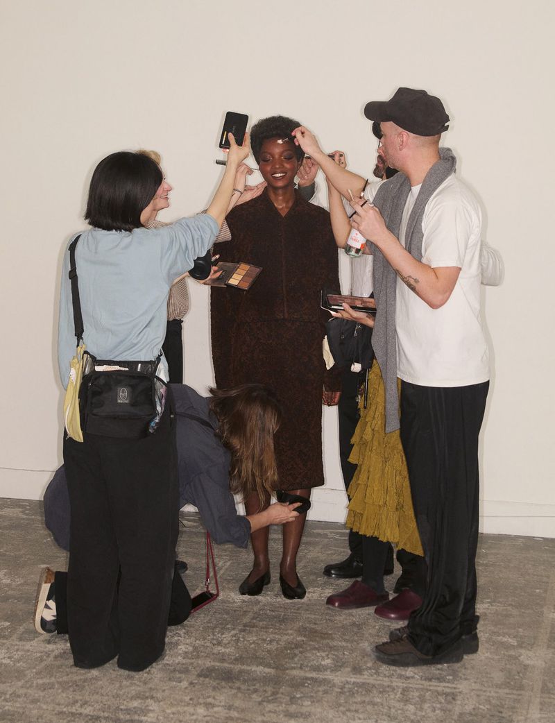 Group of crew members styling a model in a dark dress against a plain studio background.