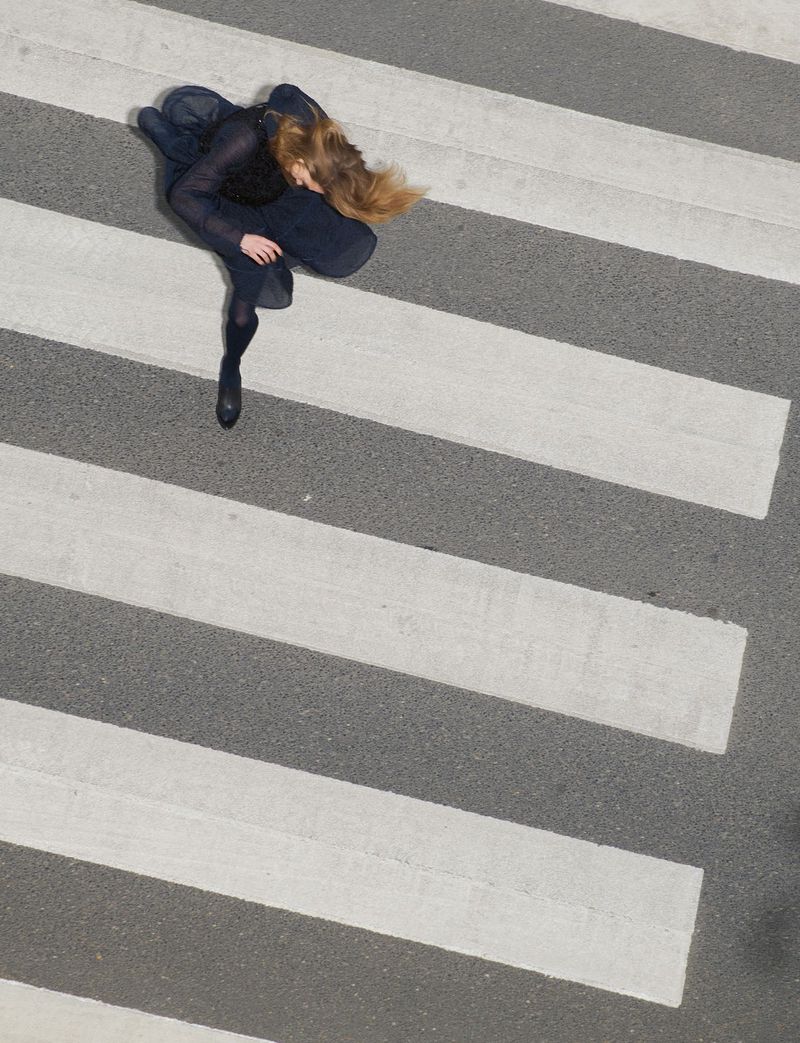 High-angle shot of a woman in a dark dress walking across a pedestrian crosswalk