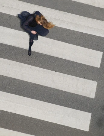 High-angle shot of a woman in a dark dress walking across a pedestrian crosswalk
