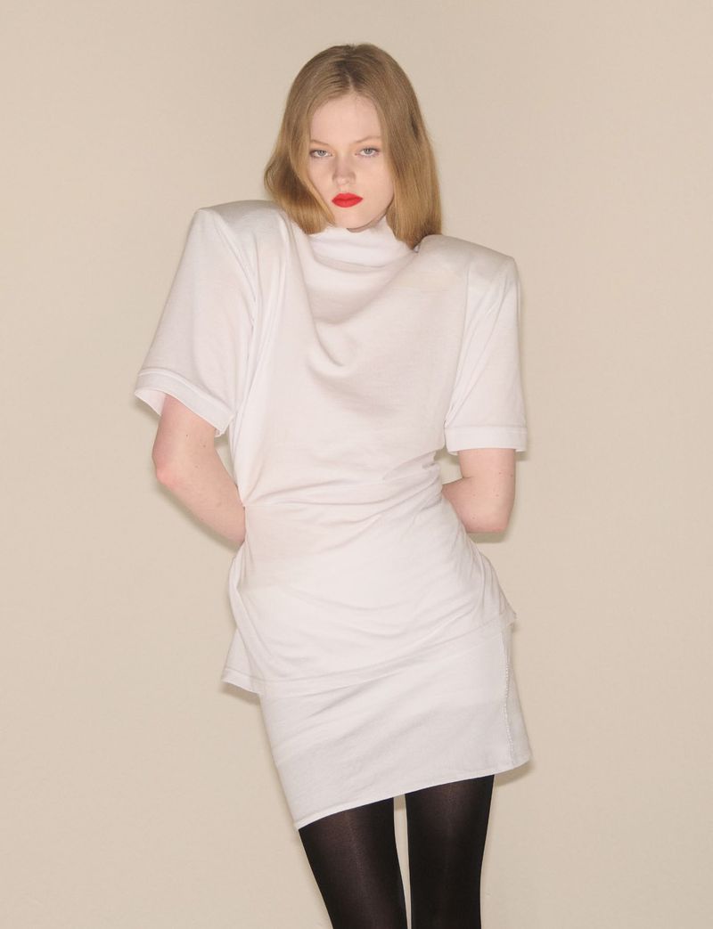 Model in a structured white top with padded shoulders and black tights against a neutral background