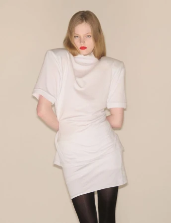 Model in a structured white top with padded shoulders and black tights against a neutral background