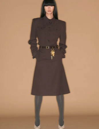 Model standing in a brown belted dress against a plain tan backdrop for System Collections Autumn Winter 2026-2027.
