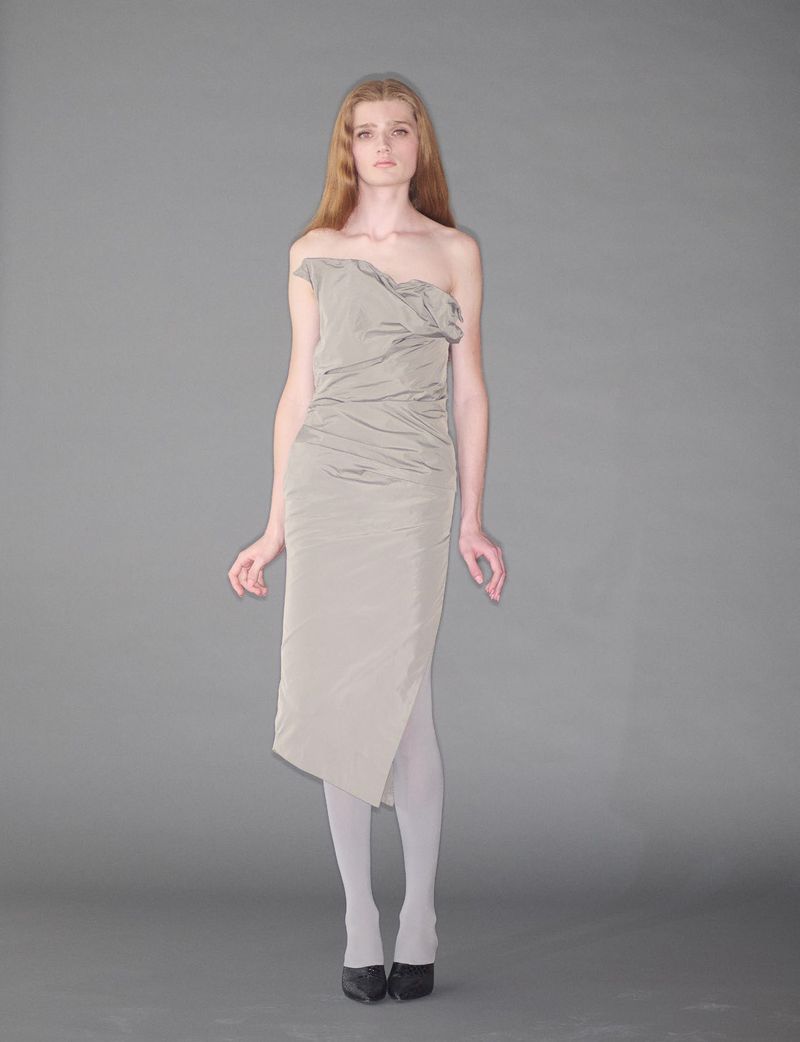 Model standing on a grey seamless background wearing an off-the-shoulder grey dress and white tights.