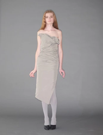 Model standing on a grey seamless background wearing an off-the-shoulder grey dress and white tights.