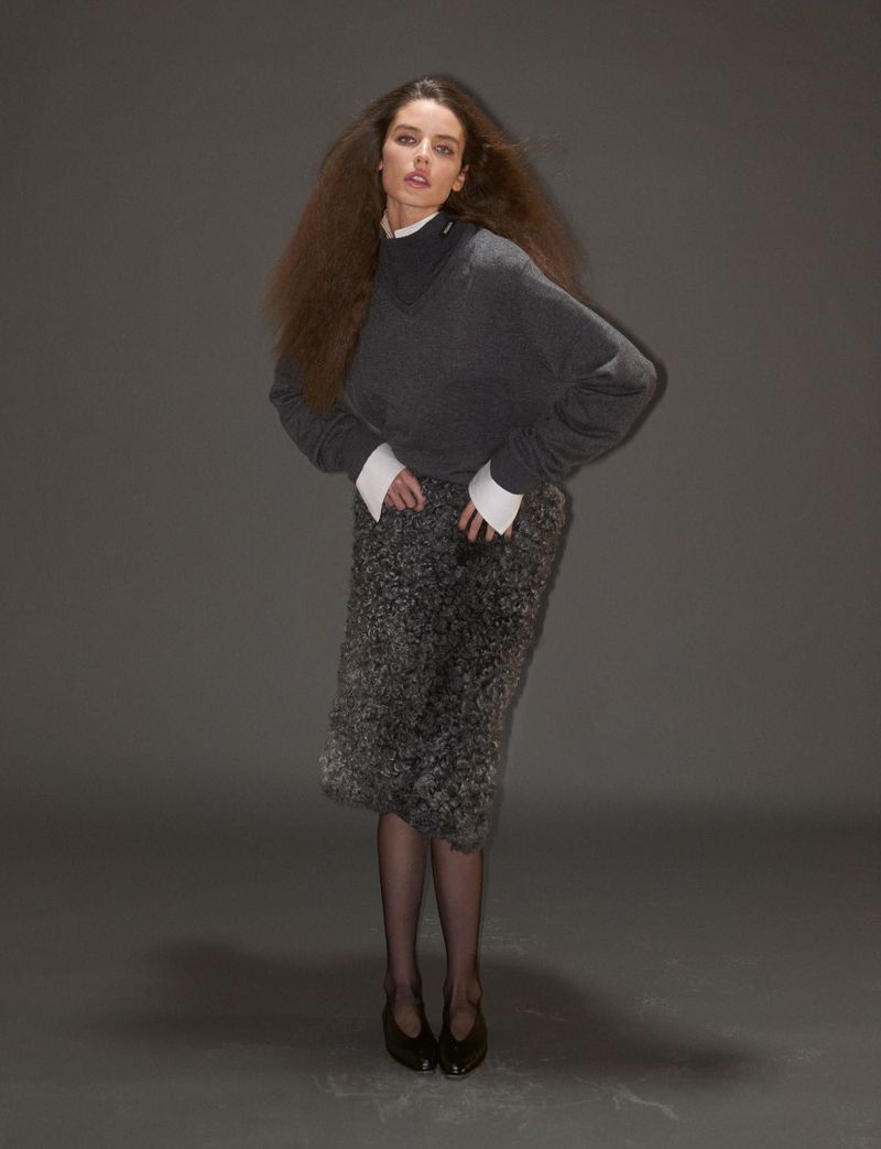 Model wearing a dark grey knit sweater and textured skirt against a neutral grey studio background