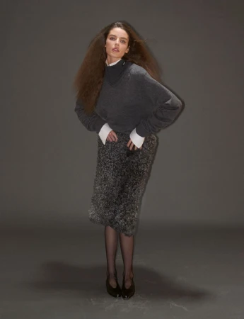 Model wearing a dark grey knit sweater and textured skirt against a neutral grey studio background