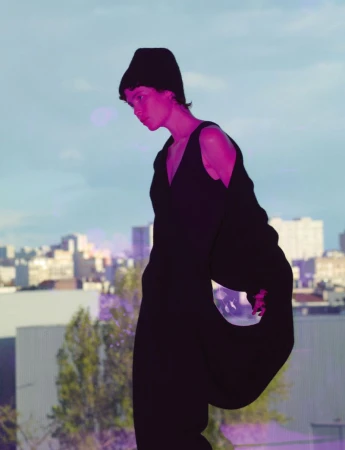 Model in dark sleeveless top and beanie against an urban skyline background