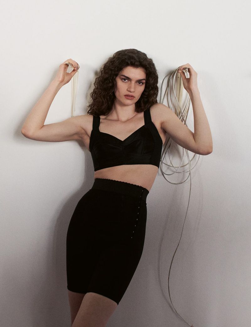 Model in black crop top and skirt holding cords against a plain white wall for System Collections Autumn Winter 2026-2027.
