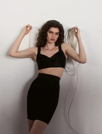 Model in black crop top and skirt holding cords against a plain white wall for System Collections Autumn Winter 2026-2027.