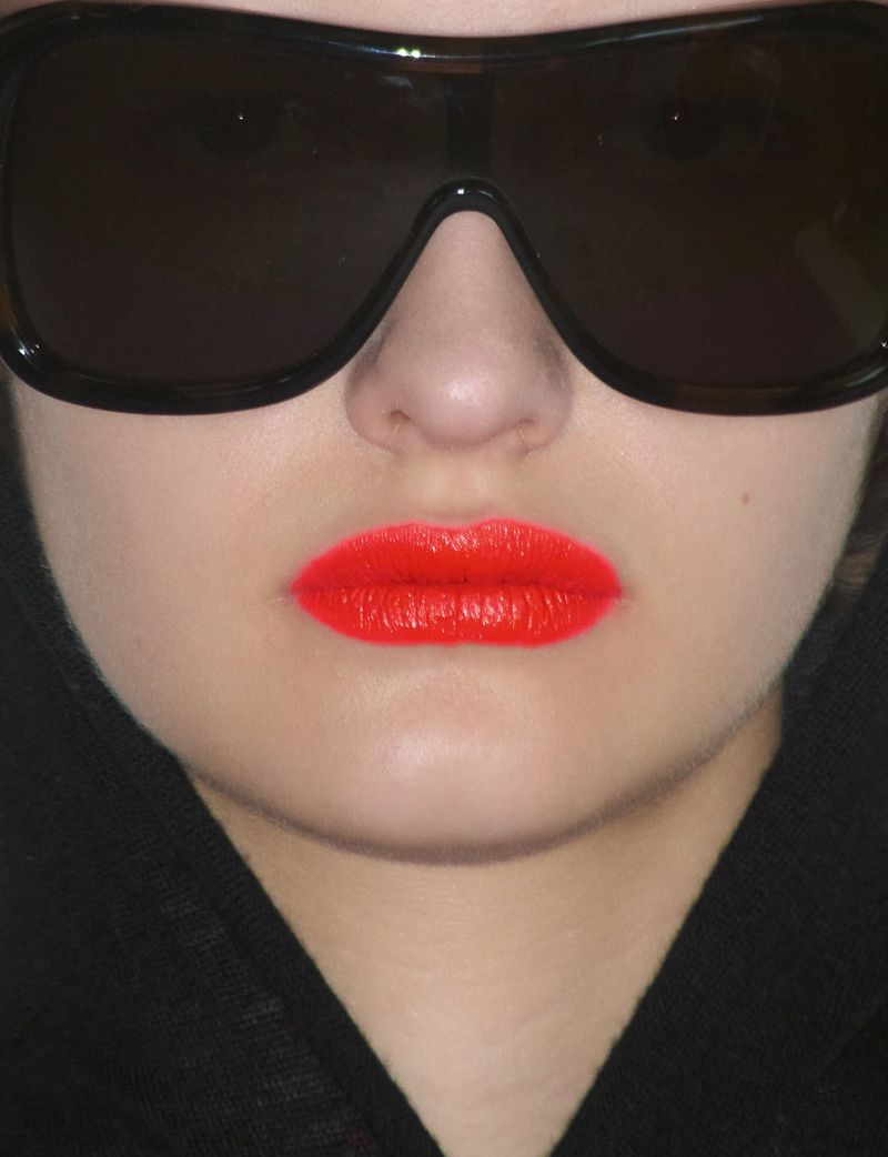 Close-up portrait of a model wearing dark oversized sunglasses and vibrant red lipstick for System Collections