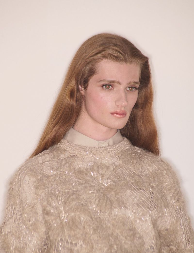 Model with long brown hair wearing a textured cream sweater against a plain white background
