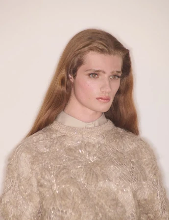Model with long brown hair wearing a textured cream sweater against a plain white background