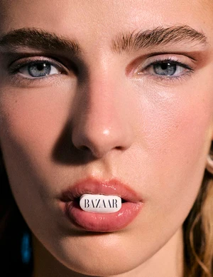 Close-up portrait of a woman holding a white pill with printed text between her lips for Harper's Bazaar Espana.