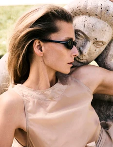 Model Hana Soukupova wearing sunglasses and a beige top beside a stone statue for Harper's Bazaar Espana