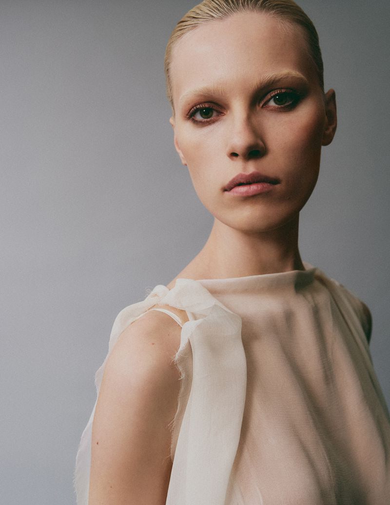 Close-up portrait of a female model wearing a cream-colored top against a solid grey background for Flaunt project Are You Feeling What I’m Feeling?