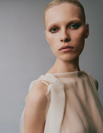 Close-up portrait of a female model wearing a cream-colored top against a solid grey background for Flaunt project Are You Feeling What I’m Feeling?