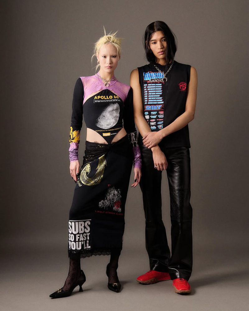 Two fashion models strike poses in a studio wearing unique streetwear ensembles with bold graphic designs and edgy, contemporary flair.