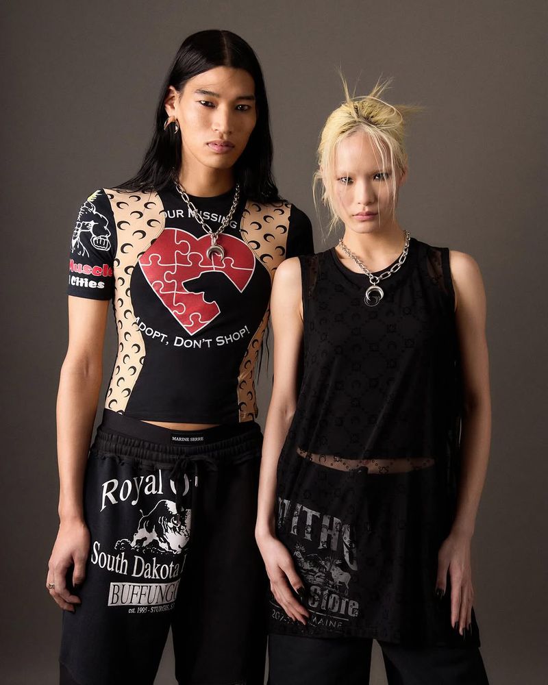 Two fashion models pose in black graphic tops and sweatpants against a grey background, showcasing contemporary streetwear style.