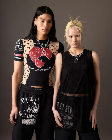 Two models posing in graphic Marine Serre tops, black bottoms, and crescent moon necklaces against a neutral grey studio backdrop.