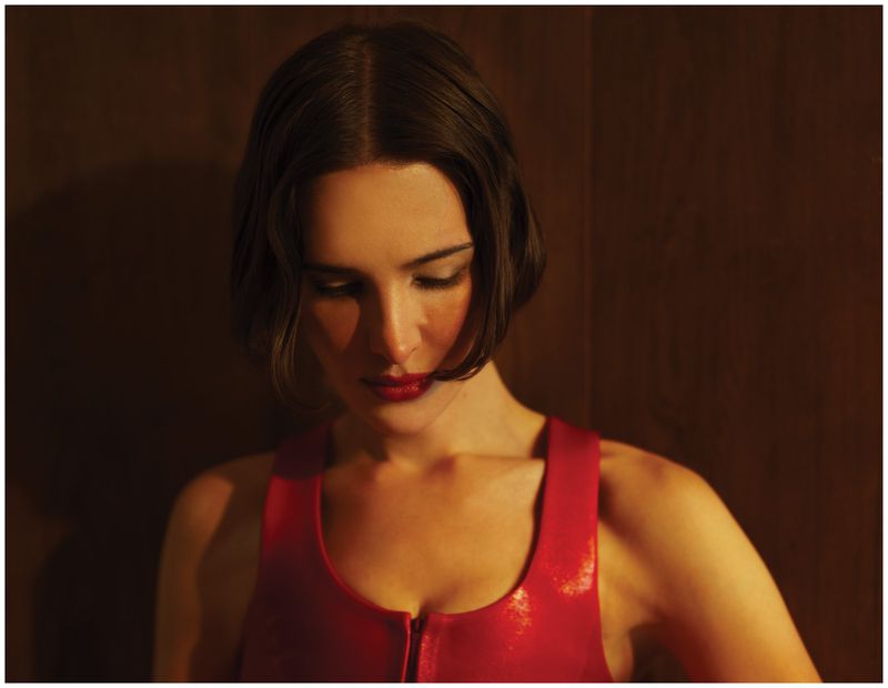 Portrait of Hari Nef wearing a red top against a dark wood wall for Schön Magazine.