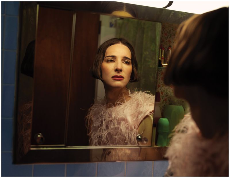 Hari Nef wearing a pink feathered top looking in a bathroom mirror for Schön Magazine