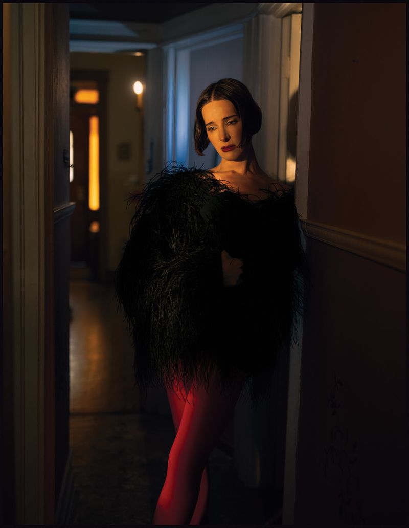 Hari Nef in a black feather garment standing in a dimly lit hallway for Schon Magazine