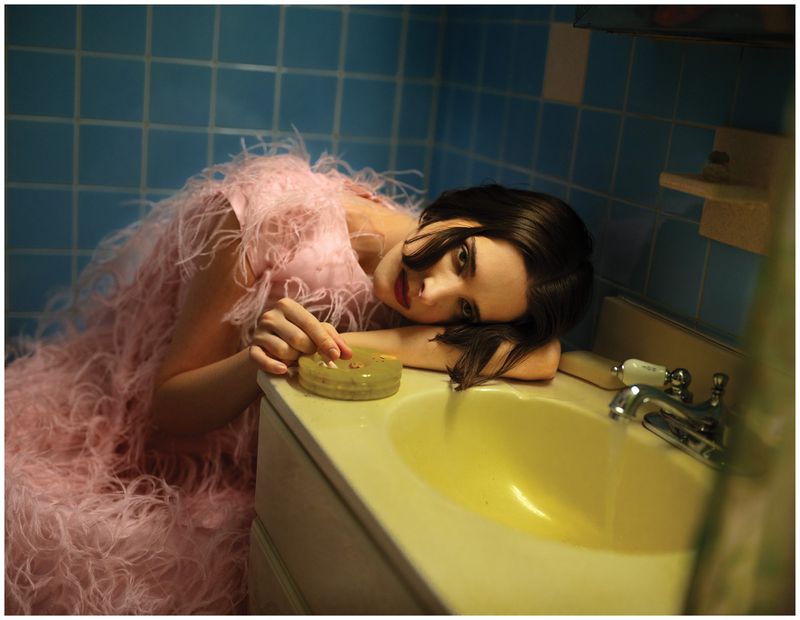 Hari Nef wearing a pink feathered dress resting her head near a sink in a blue tiled bathroom for Schön Magazine
