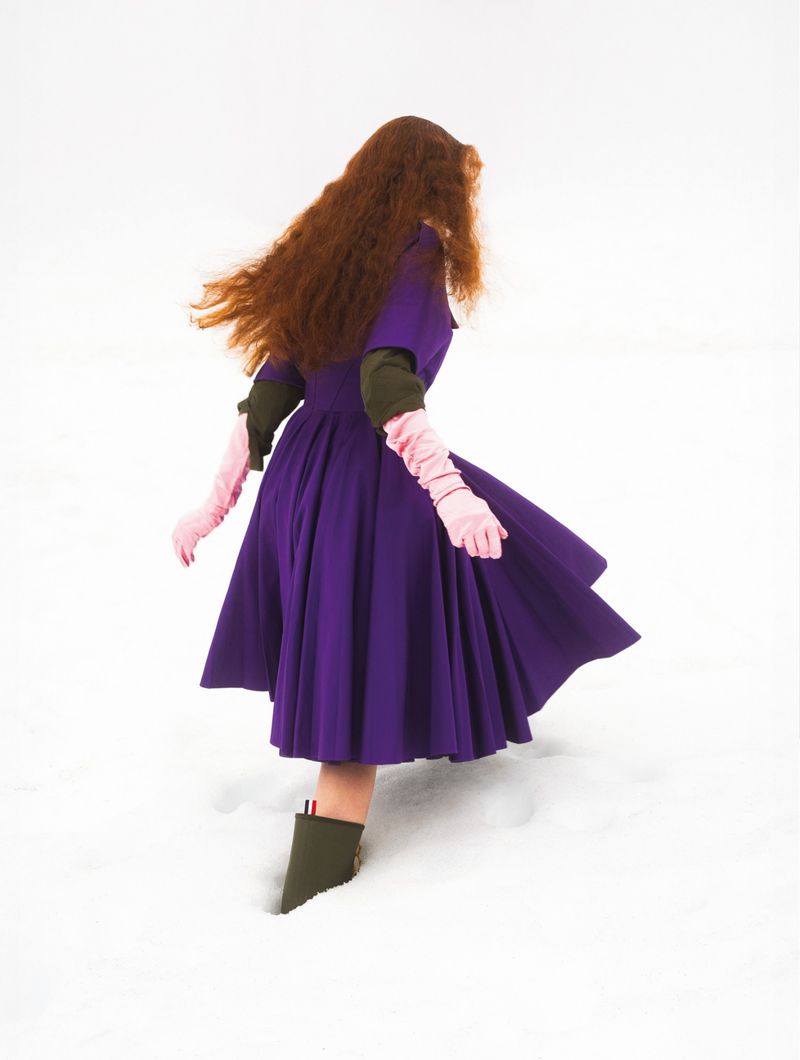 Model with long red hair wearing a purple dress and pink gloves walking in the snow for L'Officiel Italia