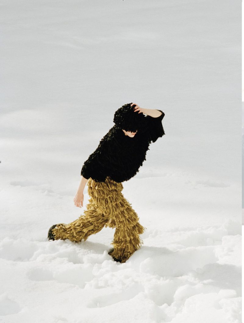 Model in textured black top and fringed gold trousers walking across a snowy field for L'Officiel Italia.