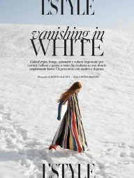 Model with long red hair wearing a colourful striped maxi dress walking across a snowy landscape.