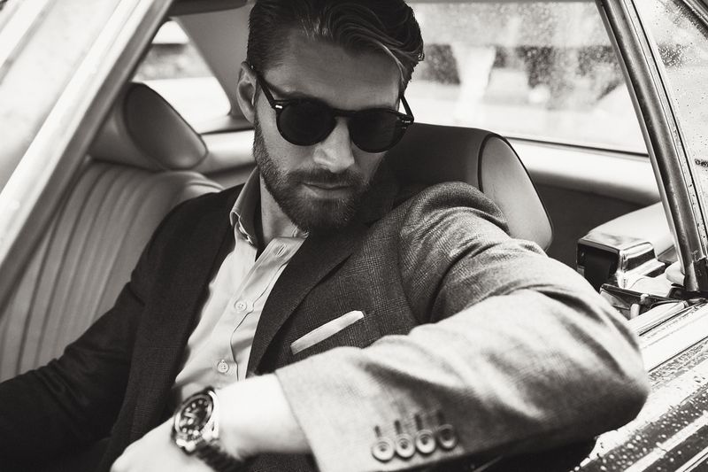 Monochrome portrait of a man in a tailored blazer and sunglasses seated inside a classic car for Thomas Pink