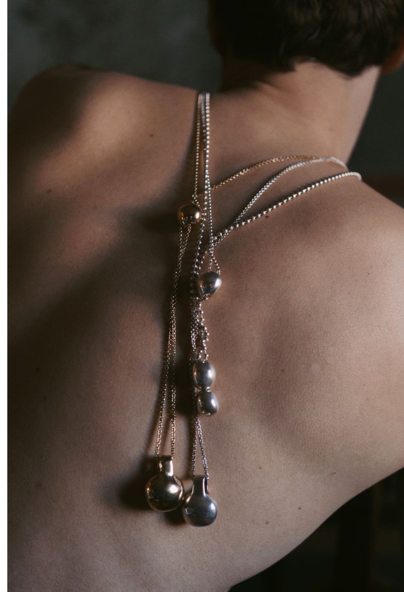 Close-up back view of a person wearing multiple silver and gold necklaces with pendant charms for Numero Netherlands.
