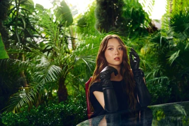 Laufey seated amidst lush tropical foliage wearing black leather gloves for Billboard Magazine