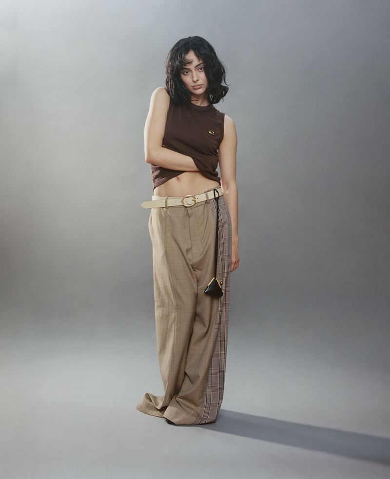 Model Aubri Ibrag wearing a brown sleeveless top and wide-leg trousers against a grey seamless studio backdrop.