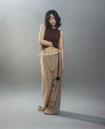Model Aubri Ibrag wearing a brown sleeveless top and wide-leg trousers against a grey seamless studio backdrop.