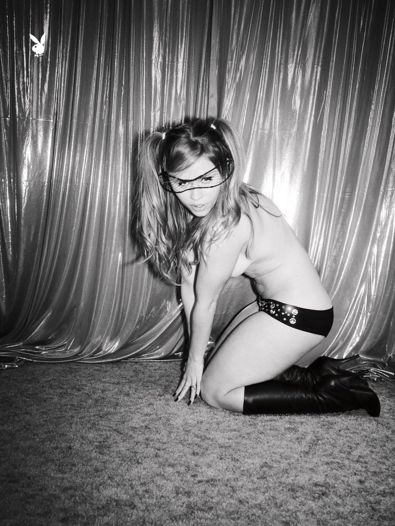 Model Lexee Smith kneeling in black briefs and knee-high boots against a shiny curtain backdrop