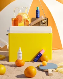 Commercial product photography of Sephora skincare bottles on a yellow cooler with oranges and beach props on sand