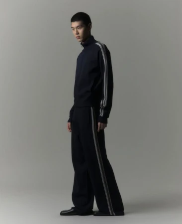 Model Jiho Kim wearing a dark navy zip track jacket and wide-leg striped track pants against a plain grey studio backdrop.