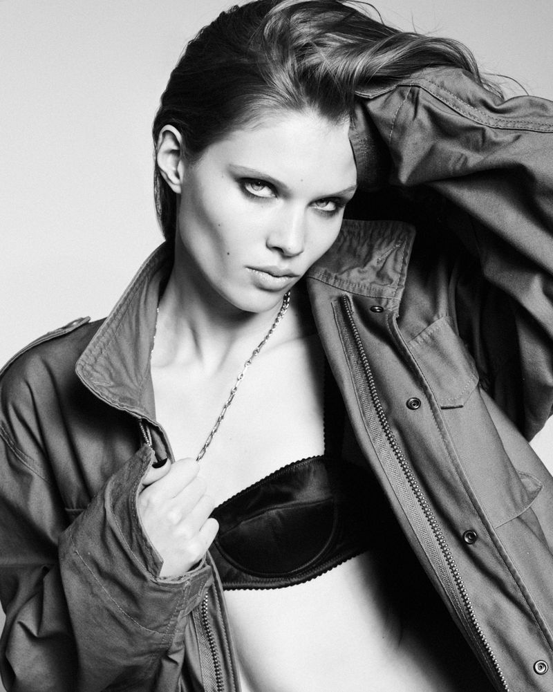 Model Ida Heiner posing in an oversized jacket and dark bra against a plain seamless white backdrop in a black and white portrait.