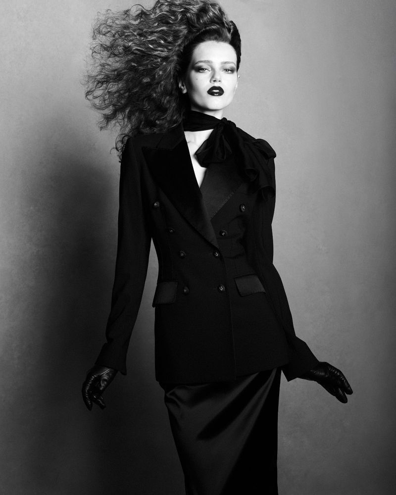 Model Charlotte Boggia with voluminous hair wearing a dark double-breasted jacket and gloves in a monochromatic fashion portrait.
