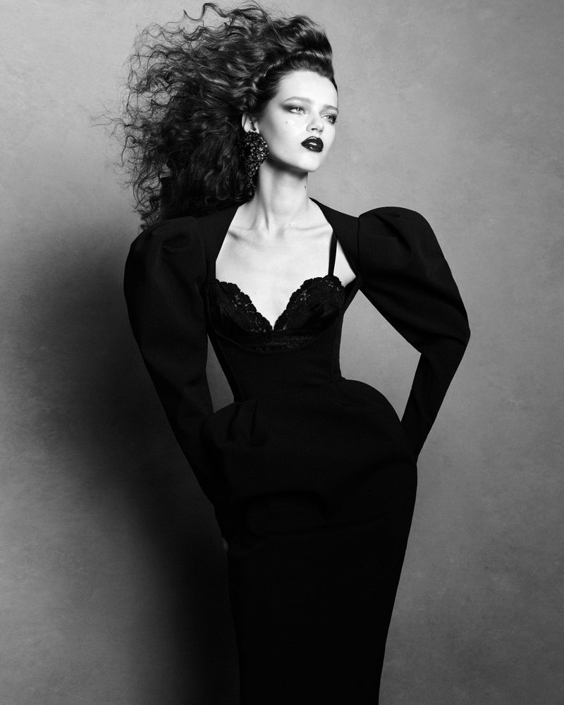 Model Charlotte Boggia with voluminous dark hair wearing a black sculptural dress against a grey studio backdrop