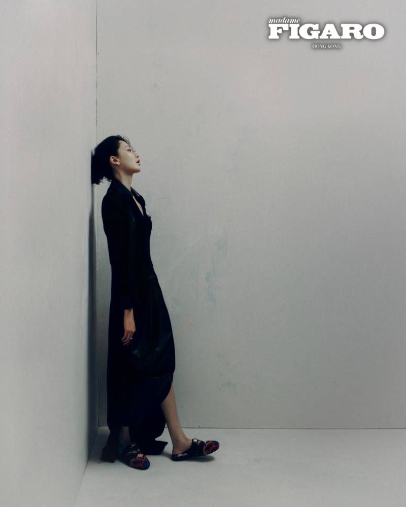 Woman in dark black dress leaning against a plain grey wall for a Madame Figaro Hong Kong fashion editorial.