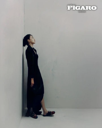 Woman in dark black dress leaning against a plain grey wall for a Madame Figaro Hong Kong fashion editorial.
