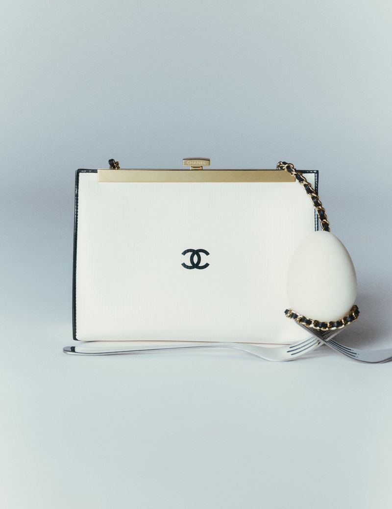 White Chanel handbag with gold hardware displayed with a white egg and silver fork on a seamless grey backdrop