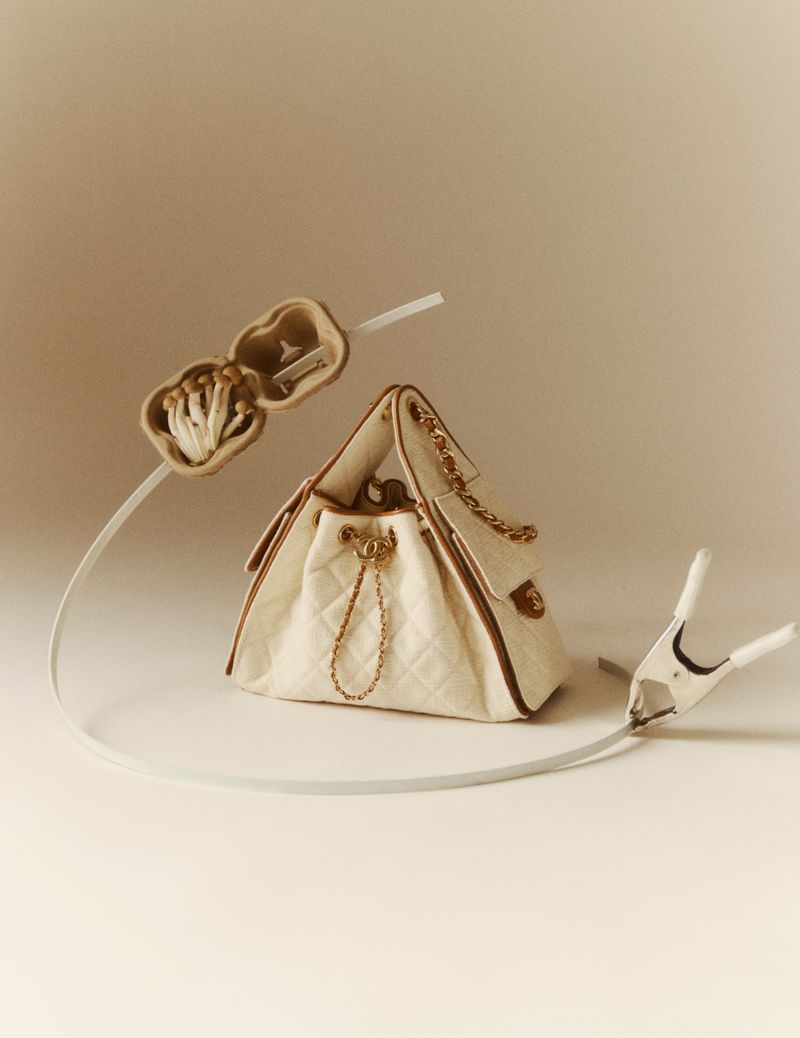 Quilted cream handbag with gold chain strap displayed on seamless neutral background with mushrooms and spring clip