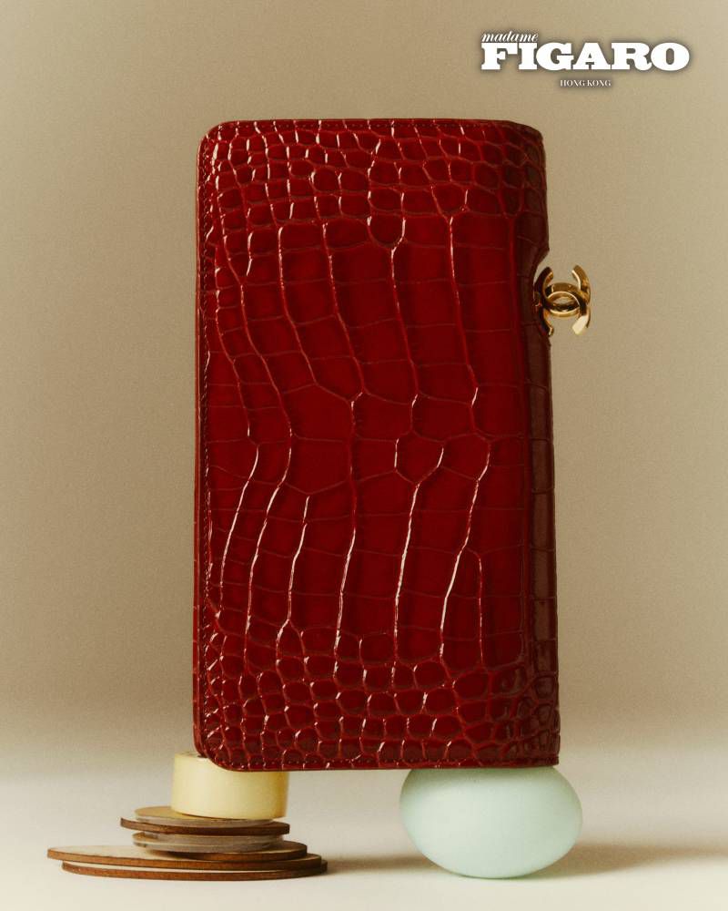 Glossy red crocodile embossed leather clutch standing on small rounded objects against a neutral background