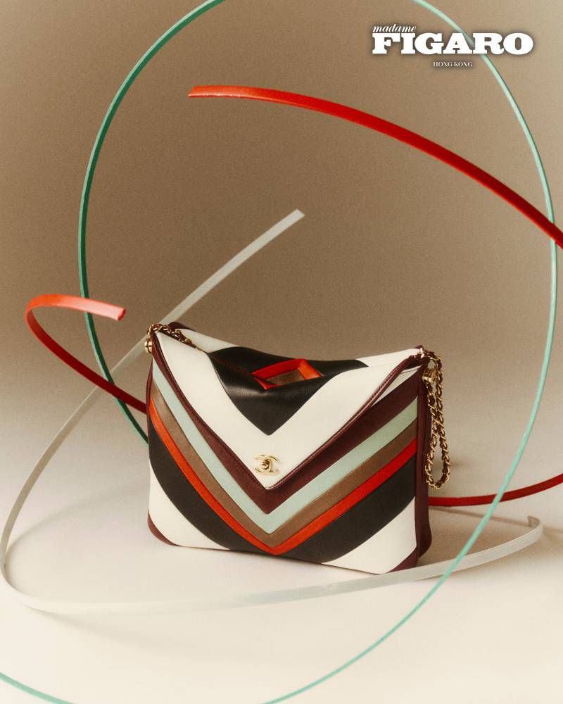 Multicolor chevron leather handbag displayed on a seamless backdrop with curved abstract sculptural wire loops.