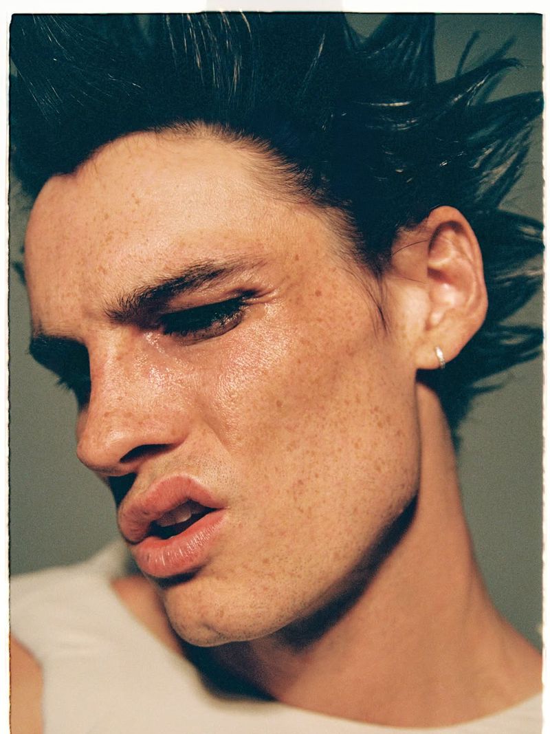 Close-up portrait of a male model with spiky dark hair and freckles wearing a white top for Numero Netherlands.