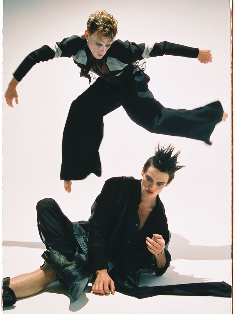 Two models in dark clothing posing dynamically against a plain white background, captured in a Numero Netherlands fashion editorial.